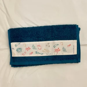 Serviette invités en éponge bleue illustrée de fruits et légumes imprimés sur une toile en coton